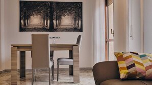 A dining area with a wooden table and chairs, a large black and white forest-themed painting on the wall, and a colorful cushion on a brown sofa. - Casa Vacanze Asariel Splendido Appartamento Vista Mare e Centro Città (Brindisi)