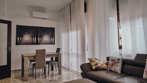 A modern living room with a brown leather sofa, a wooden dining table with two chairs, and a large abstract painting on the wall. - Casa Vacanze Asariel Splendido Appartamento Vista Mare e Centro Città (Brindisi)