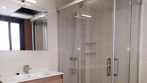 Ein modernes Badezimmer mit einer gläsernen Duschkabine, einem weißen Waschbecken und einem Holzlagerplatz.
