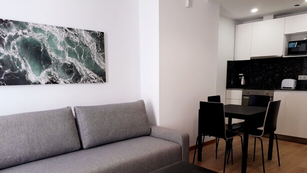 Ein modernes Wohnzimmer mit einem grauen Sofa, einem schwarzen Couchtisch und einer Küchenzeile mit schwarzer Arbeitsplatte und weißen Schränken.