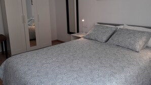 Ein Schlafzimmer mit Bett, Schrank, Nachttisch, Spiegel und zwei gerahmten Bildern an der Wand.