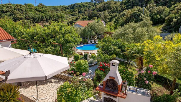 A pool surrounded by lush greenery, a barbecue area, and a white building with a red roof. - Amazing apartment in Mundanije (Mundanije)