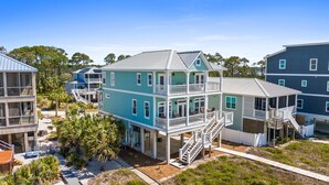 A multi-story coastal house with balconies, a covered porch, and a sandy driveway.