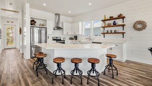 A modern kitchen with a central island, bar stools, white cabinetry, and a stainless steel refrigerator.
