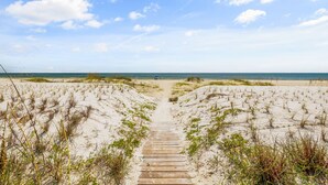 A sandy beach path leading to the ocean with dunes on either side.