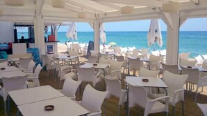 Zona pranzo all'aperto con tavoli e sedie bianche, con vista sul mare.