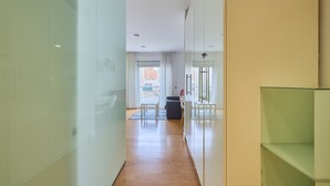 Un corridoio moderno con pareti in vetro, pavimento in legno e vista sulla città attraverso ampie finestre.