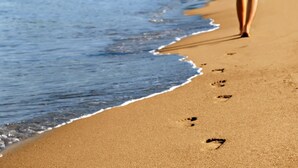 Una spiaggia sabbiosa con impronte che si perdono nell'acqua.