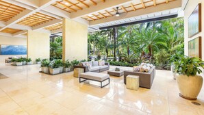 A spacious lobby with a high ceiling, large windows, and a view of tropical greenery. - Ocean-City Views Glamorous Condo at The Watermark w/Parking & Full Kitchen (Honolulu)