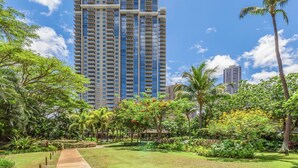 A tall hotel with a modern design, surrounded by lush greenery and palm trees. - Ocean-City Views Glamorous Condo at The Watermark w/Parking & Full Kitchen (Honolulu)