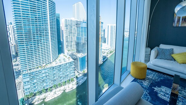 A high-rise hotel room with a large window offering a view of a city skyline and a river. - Breathtaking view (Miami)