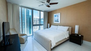 A modern hotel room with a large bed, a flat-screen TV, a desk, and a view of the cityscape through large windows. - Breathtaking view (Miami)