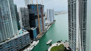 A high-rise building with a construction crane, a marina with yachts, and a waterfront promenade. - Breathtaking view (Miami)