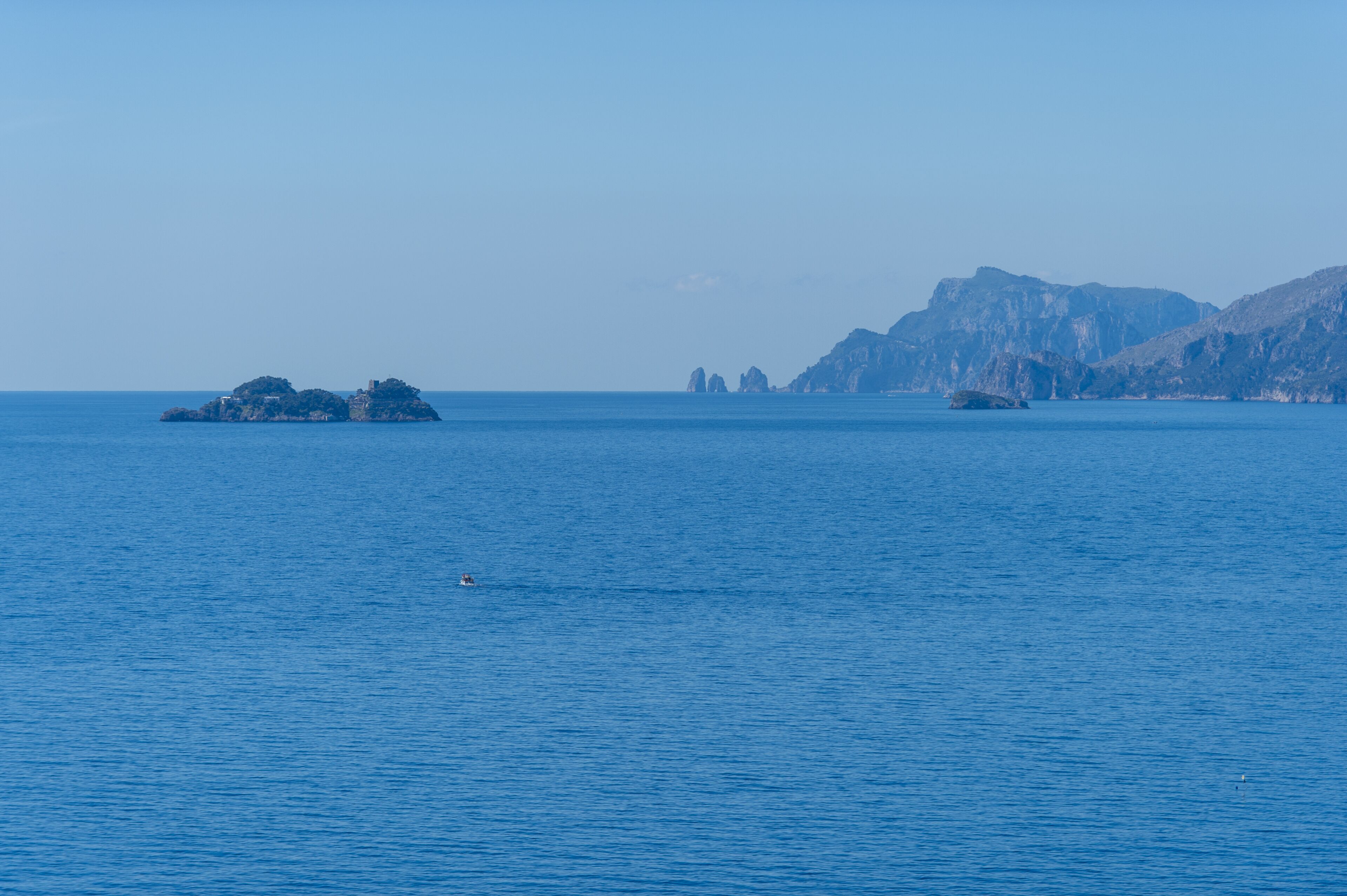 Un mar tranquilo con una pequeña isla y acantilados rocosos a lo lejos.