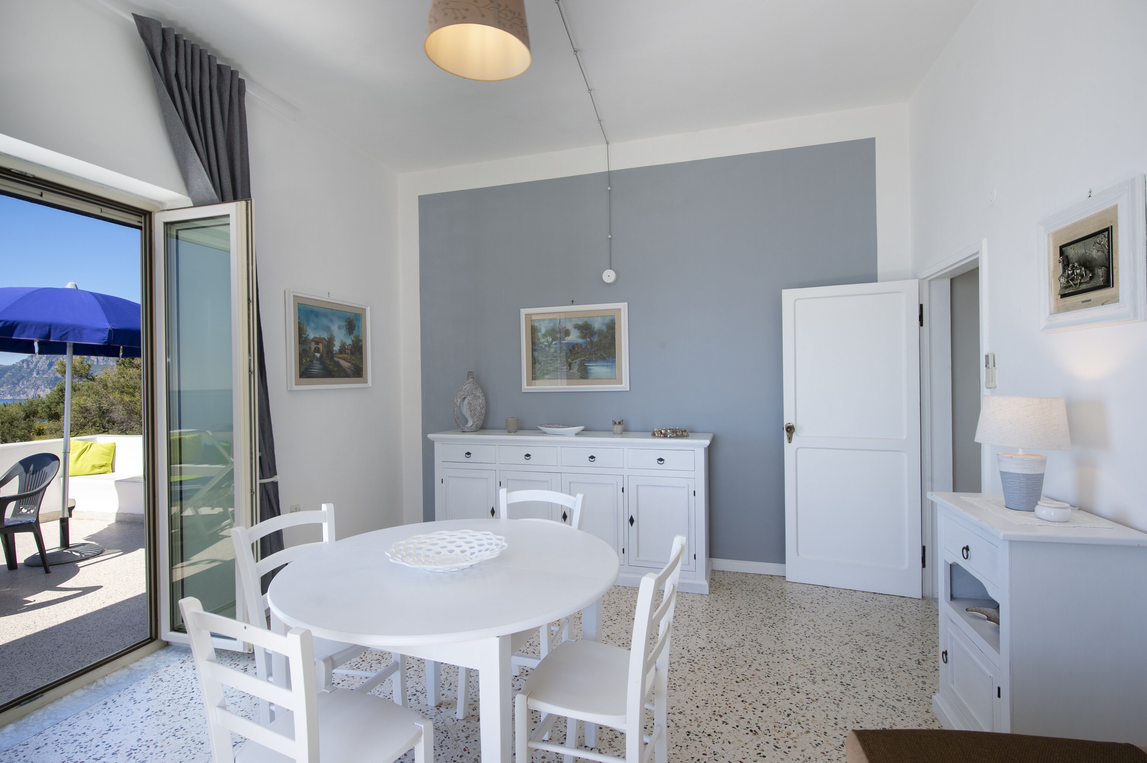 Una cocina moderna con armarios blancos, una mesa de comedor con sillas y vistas al exterior a través de un ventanal corredera.