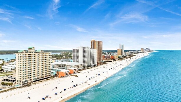 A coastal cityscape with a beachfront hotel, high-rise buildings, and a clear blue sky. - Crystal Shores1006 2 Bedroom Condo by RedAwning (Gulf Shores)