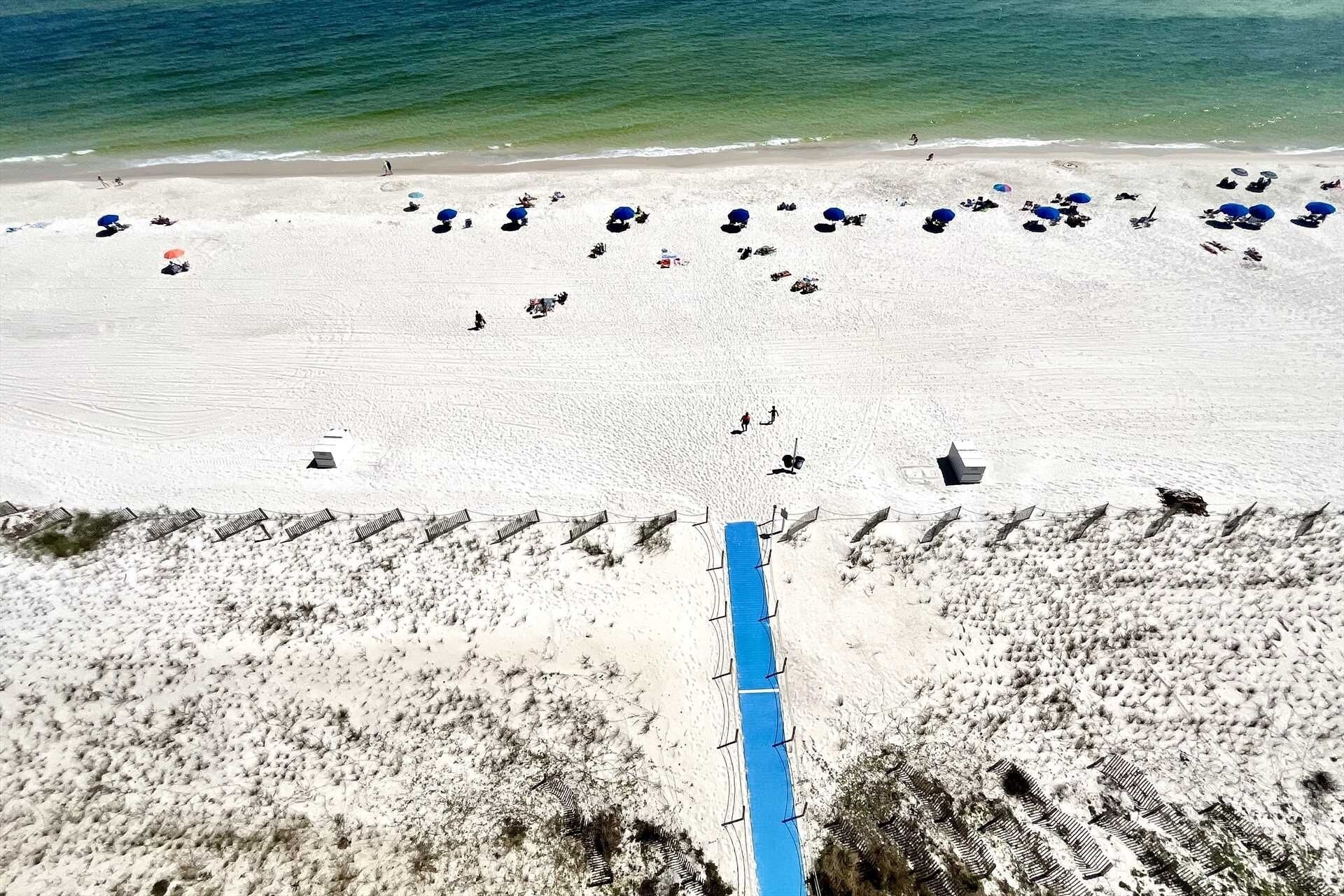A beach with a blue pathway leading to the water, white sand, and several umbrellas.