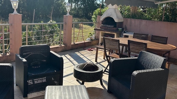 An outdoor patio with wicker furniture, a barbecue grill, and a pergola providing shade.
