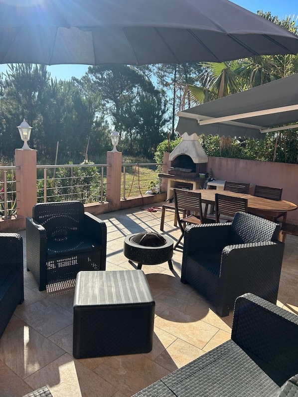 An outdoor patio with wicker furniture, a barbecue grill, and a pergola providing shade.