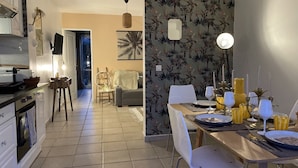 A dining area with a table set for four, a kitchen in the background, and a living room with a sofa and a TV.
