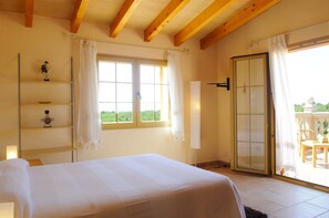 A bedroom with a bed, a window with curtains, a sliding glass door to a balcony, and wooden beams on the ceiling. - Beautiful house for 6 people with pool, just a few minutes' drive to the beach (S' Horta)