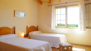 A room with two single beds, a wooden headboard, a nightstand with a lamp, a window with curtains, and a small wooden stool. - Beautiful house for 6 people with pool, just a few minutes' drive to the beach (S' Horta)