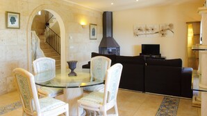 A living room with a glass table, four patterned chairs, a black sofa, a TV, and a fireplace. - Beautiful house for 6 people with pool, just a few minutes' drive to the beach (S' Horta)