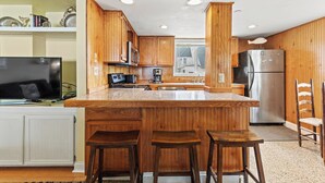 A kitchen with wooden cabinets, a stainless steel refrigerator, a large island with stools, and a window providing natural light.