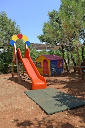 Children can play on a slide and in a playhouse surrounded by trees.