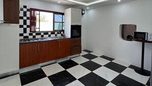 Uma cozinha moderna com piso xadrez preto e branco, armários de madeira e um micro-ondas sobre uma mesinha.