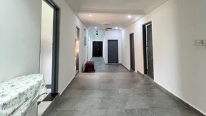 Corredor com uma cama à esquerda, uma mala no centro e uma porta no final.