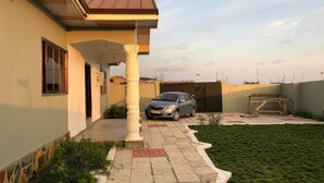 Edifício residencial com varanda coberta, um carro estacionado na entrada e um gramado.