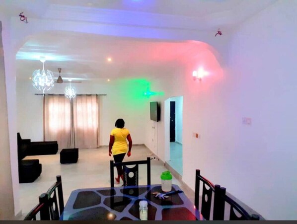 A dining area with a table and chairs, a chandelier, and a television on the wall. - Charming 4-bed House in Kokrobite (Kokrobite)