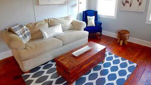 A living room with a beige sofa, a blue armchair, a wooden coffee table, and a patterned rug.