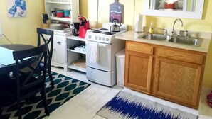 A compact kitchen with white appliances, a wooden cabinet, and a dining area with a black chair.