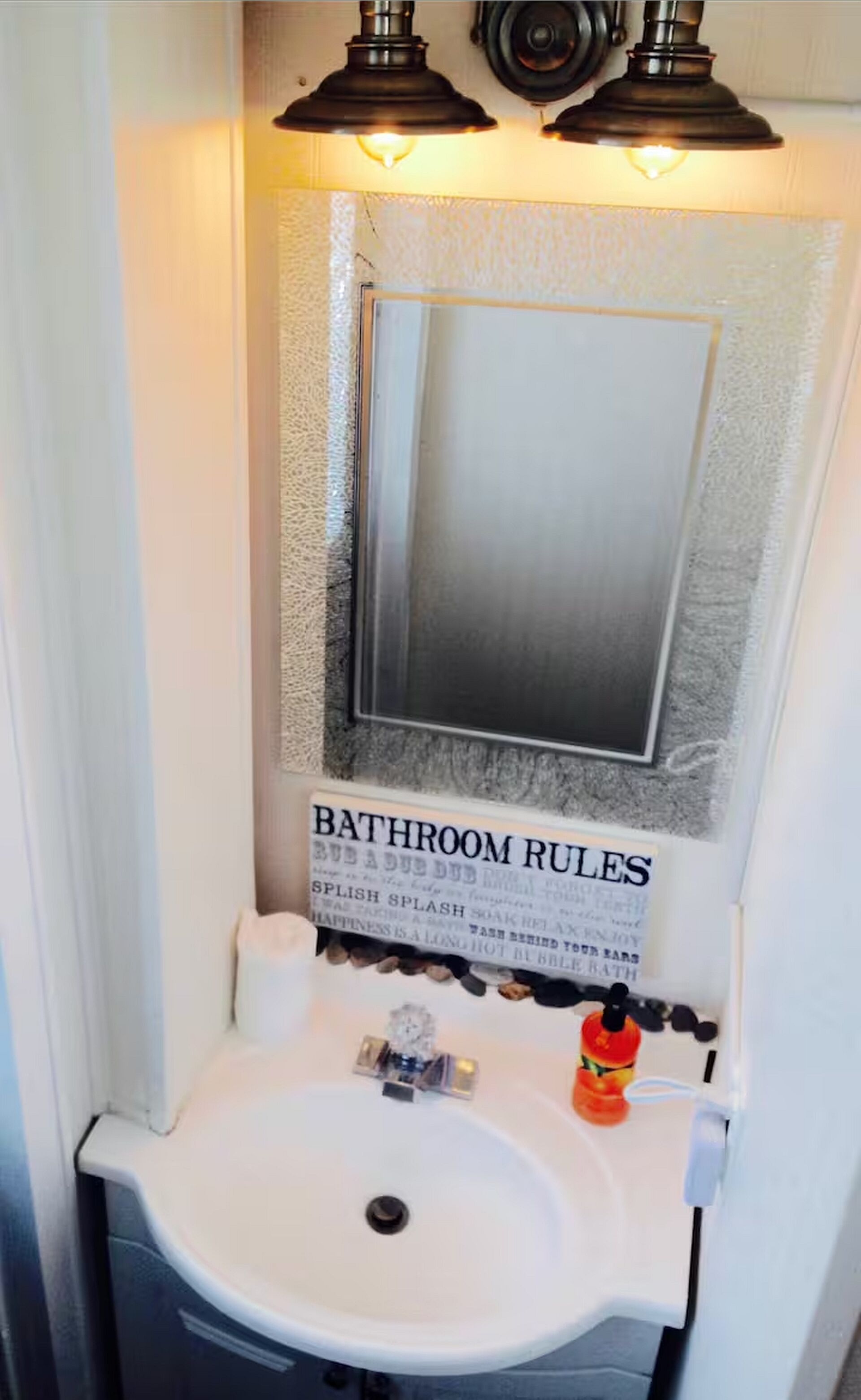 A bathroom with a white sink, two overhead lights, and a sign above the mirror stating 'BATHROOM RULES'.