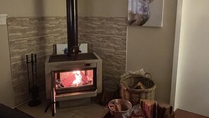 A wood-burning stove with a chimney, a fireplace, a deer artwork on the wall, and a basket with logs. - Blue Wren Retreat, Nannup - "Resting Place" (Nannup)