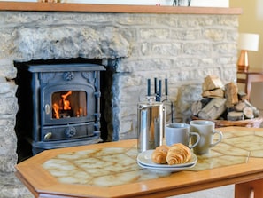 A stone fireplace with a wood-burning stove, a metal kettle, a mug, and croissants on a tiled table.