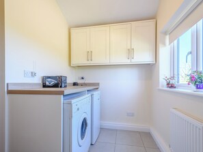A laundry area with a washing machine, a shelf with a box, and a window with plants. - 3 bedroom accommodation in Cambridge, near Lower Cam (Cambridge, near Lower Cam)