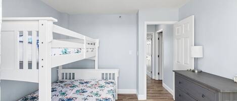 Un dormitorio con una litera, un aparador y una puerta que da a otra habitación.