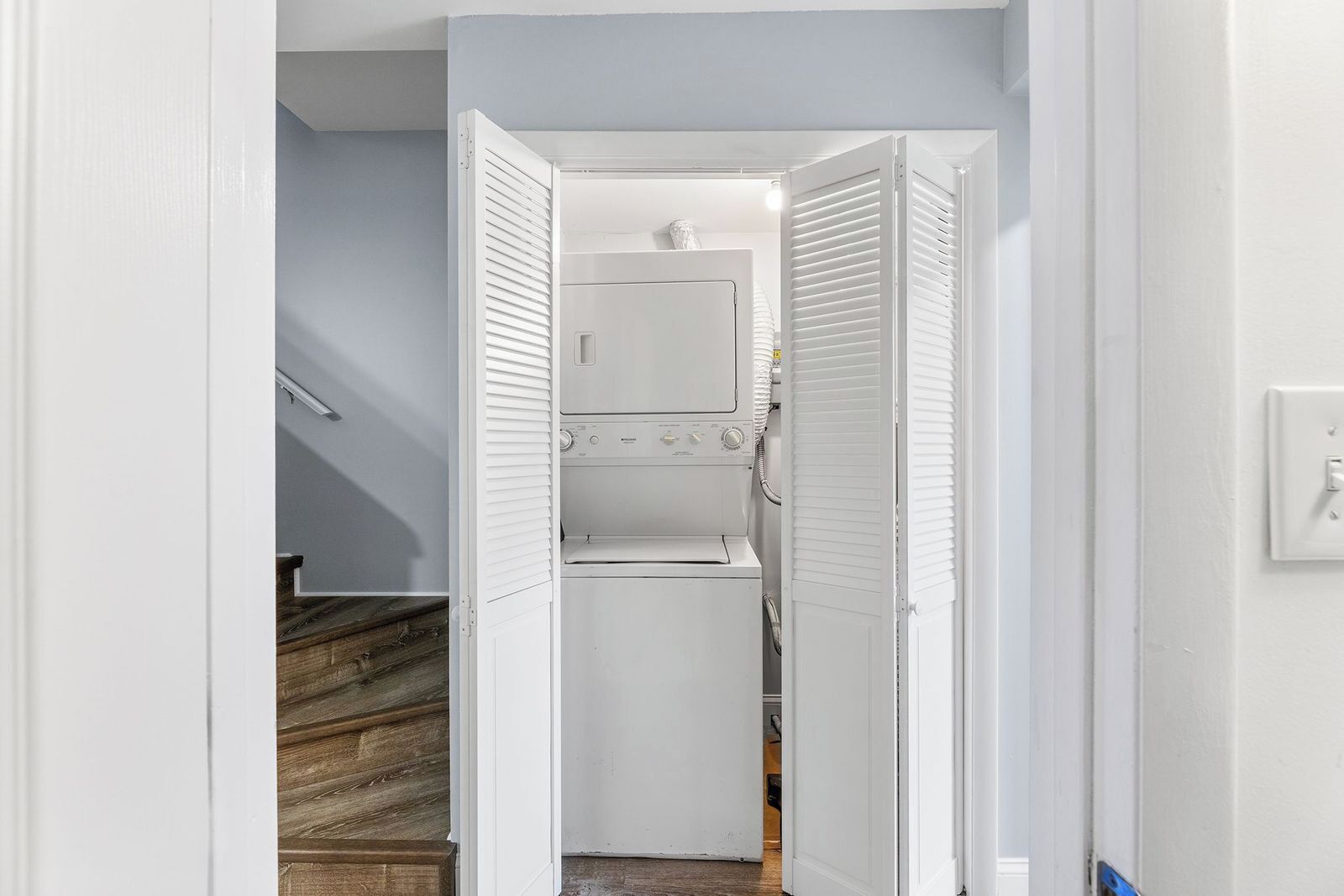 A laundry room with a washing machine and dryer, a wooden staircase, and a white door.