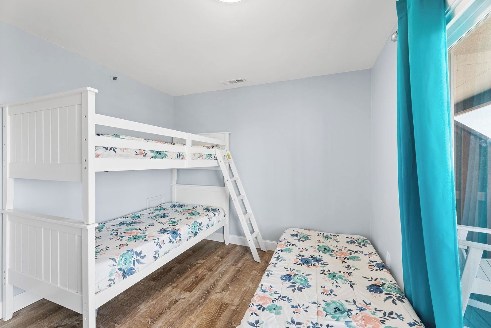 Una cama nido con ropa de cama floral, suelo de madera y una ventana con cortinas.