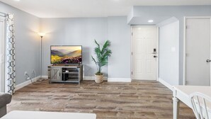 Een moderne woonkamer met een flatscreen televisie, een potplant en een witte deur.