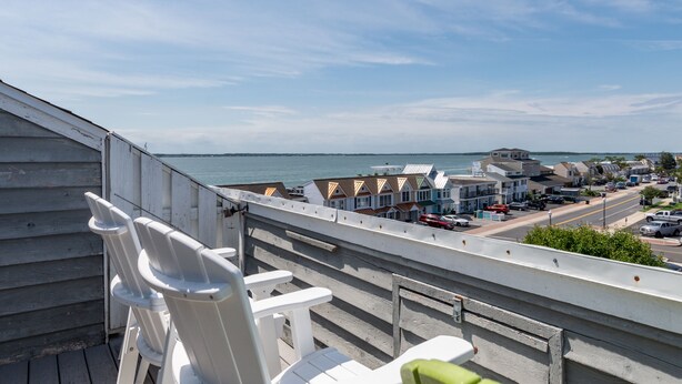 Een balkon met witte stoelen met uitzicht op een kustplaatsje en de zee.