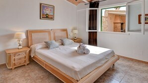 A bedroom with a wooden bed, two bedside tables, a nightstand, and a window with a view of a building.