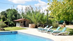 A swimming pool with lounge chairs, a small stone building, and lush greenery.