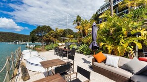 Relax by the water's edge in this serene outdoor seating area surrounded by lush greenery and a dock with boats.