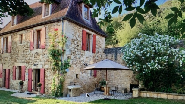 Un bâtiment en pierre avec des volets rouges, une terrasse avec du mobilier d’extérieur et un jardin.