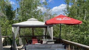 A hot tub on a wooden deck with a red umbrella and a gazebo in the background. - The Cabin on Grey Owl w/hot tub (Onanole)
