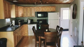 A kitchen with wooden cabinets, a dining table with chairs, a microwave, a refrigerator, and a ceiling fan. - The Cabin on Grey Owl w/hot tub (Onanole)